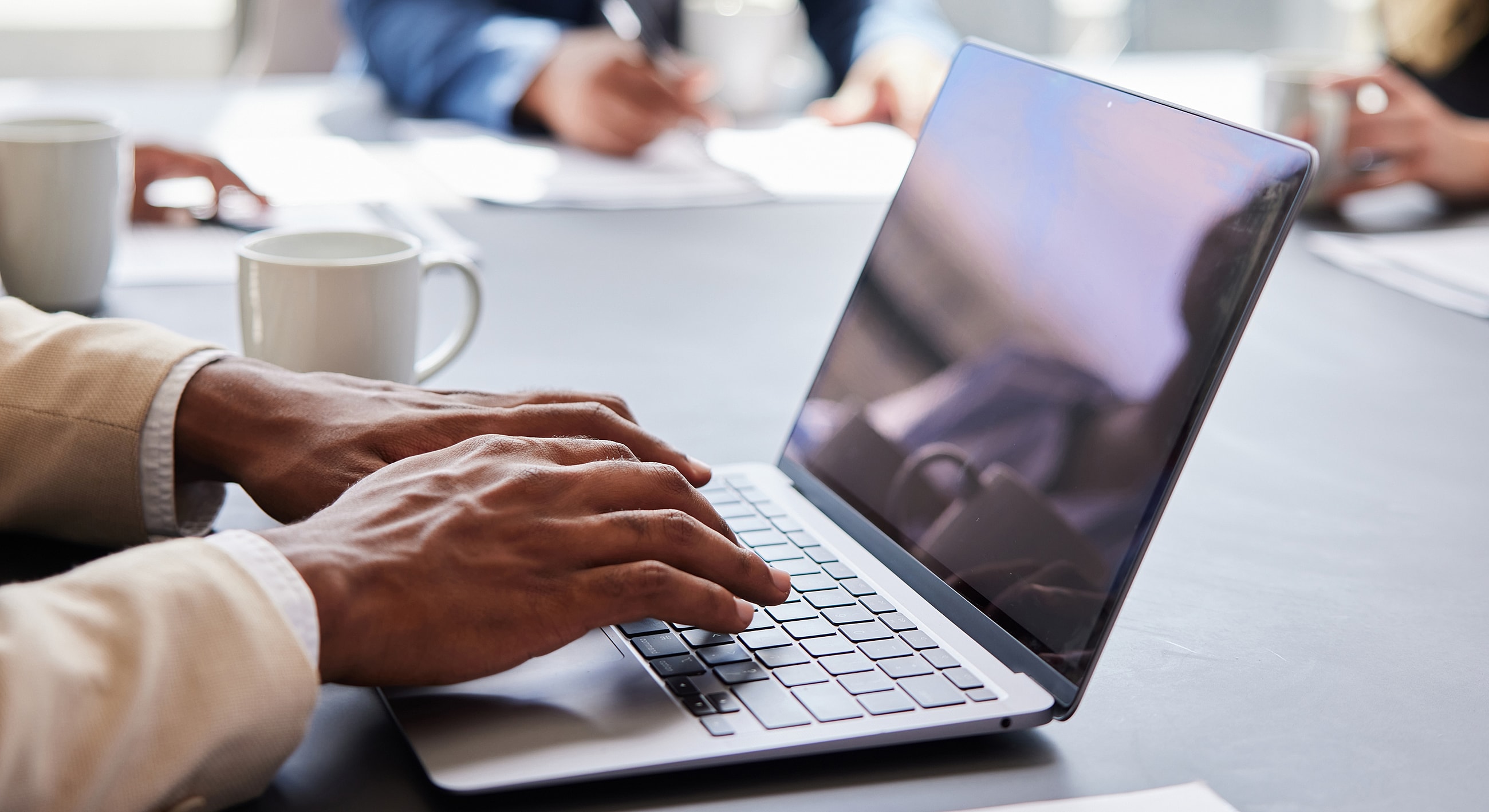 Hands typing on a laptop in a meeting.